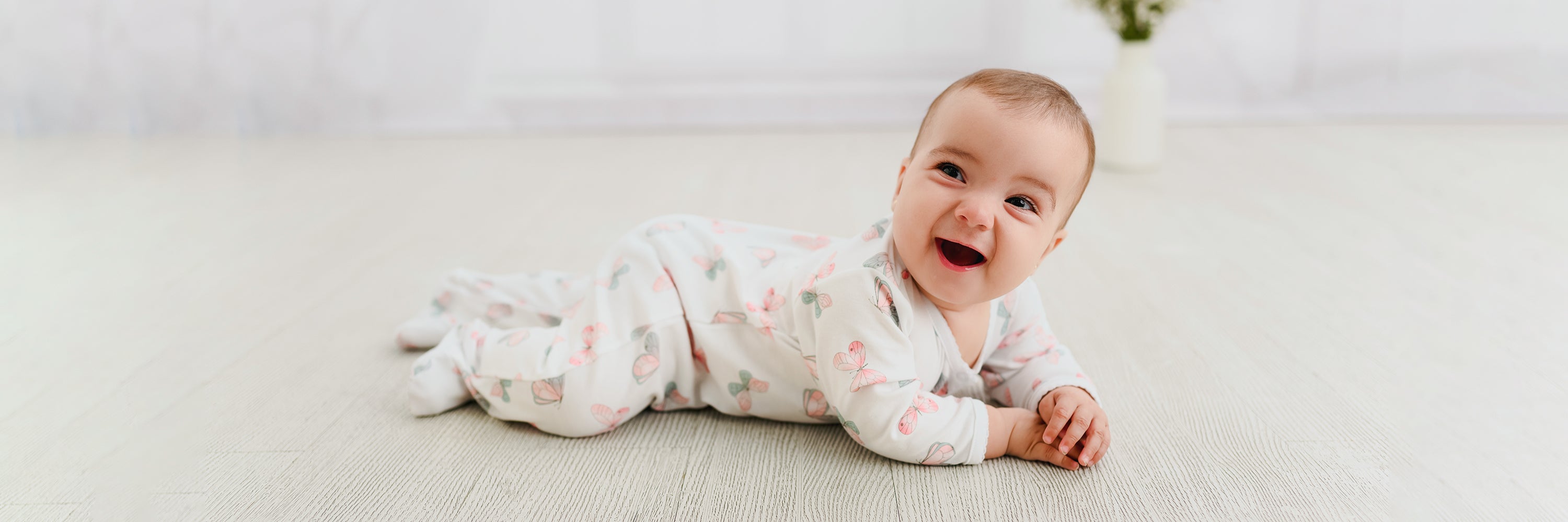 Baby girl in a Pima cotton footie happily lying on the floor