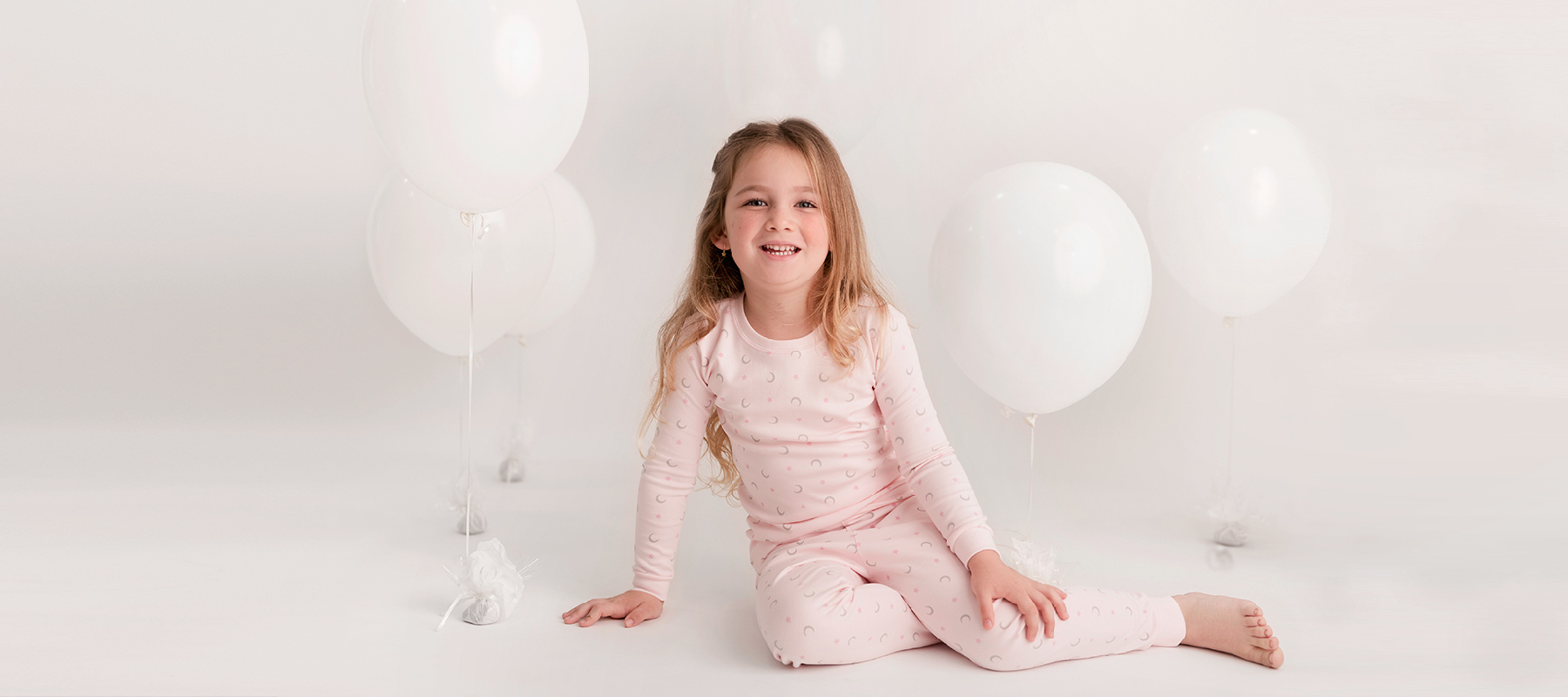 Little girl wearing Pima cotton pajamas, sitting on the floor with balloons