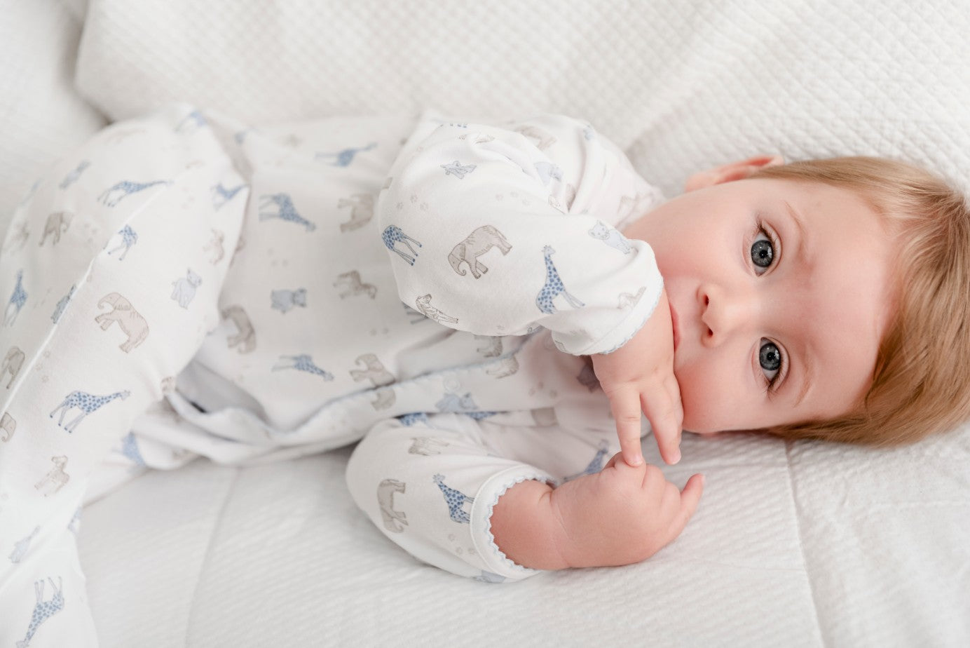Baby in Pima cotton onesie resting on white bed blanket